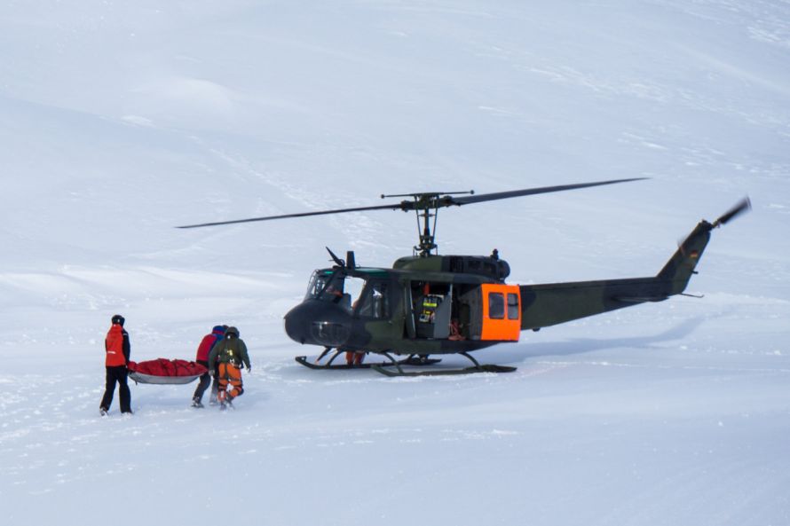 Helfer transportieren verletzten Wintersportler zu Hubschrauber